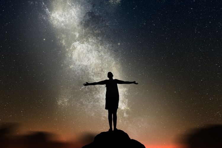 Photograph of a female silhouette standing in front of the milky way galaxy at night.