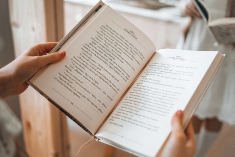 A mirror reveals a woman standing with an open book, which is centered and in focus for viewers.