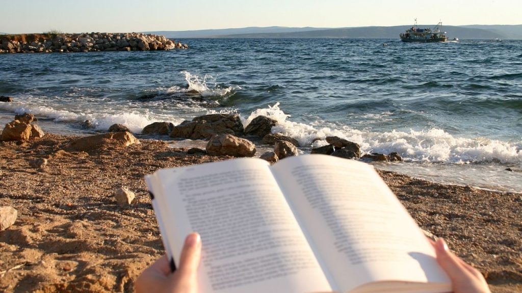 An open book being read on a sandy beach.