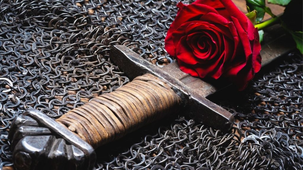 Chainmail armor with a sword and a rose resting on top of it.