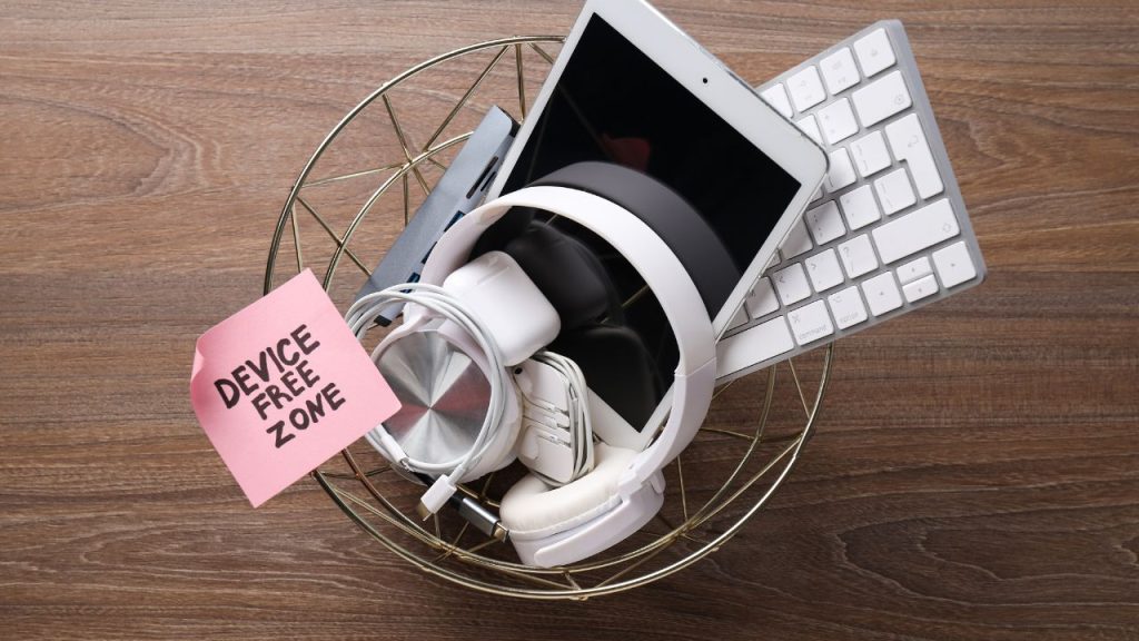 A trash bin with electronics thrown in with a sticky note that says, "Device-Free Zone."