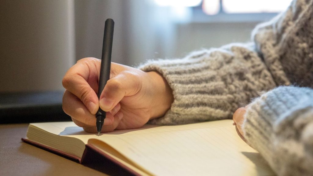 Someone writing on a hardcover notebook.