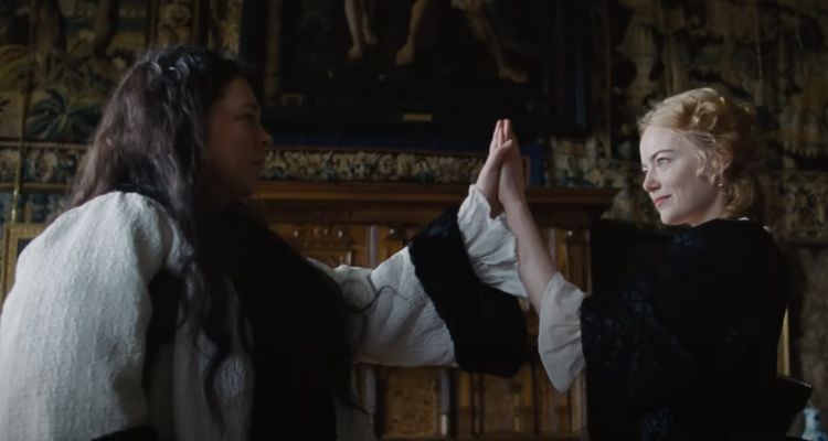 Movie still taken from The Favourite's trailer, framing Olivia Colman as Queen Anne andEmma Stone as Abigail Hill.