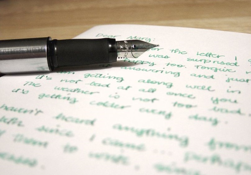 A handwritten letter in green ink with a pen resting on top