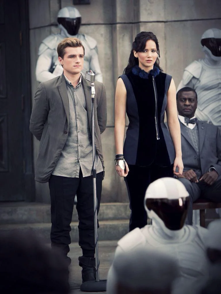Katniss and Peeta standing on a stage surrounded by Peacekeepers.