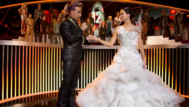 Katniss wearing her wedding dress in stage with Caesar Flickerman holding her hand