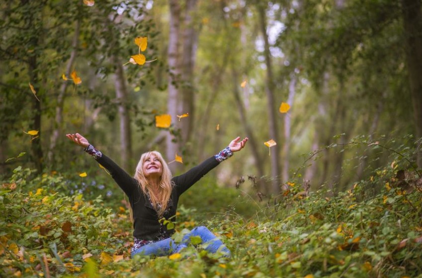 A woman sitting on the ground with her arms outstretched with a wide smile