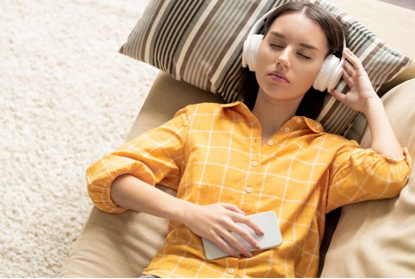 A woman lying on a couch with headphones on and her eyes closed