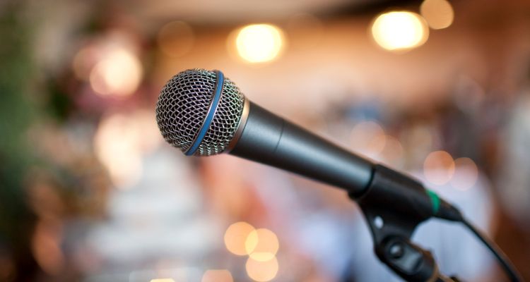 A microphone in a stand is in the center. There are blurred lights in the background.