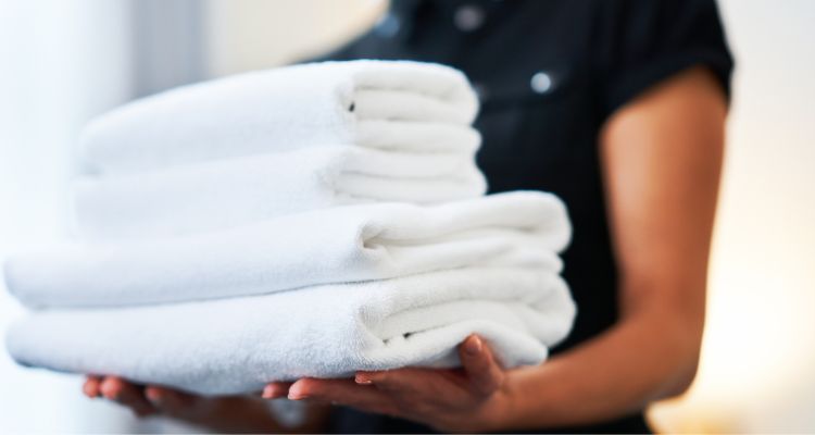 A woman in a black shirt carries 4 white towels, 2 large and 2 small.