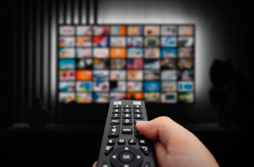 Someone holding a remote a pointing it at a TV with 56 show options