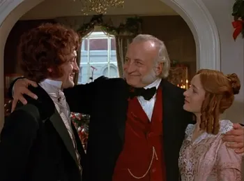 Scrooge with his arms around his nephew Fred and Fred's fiancée Bess