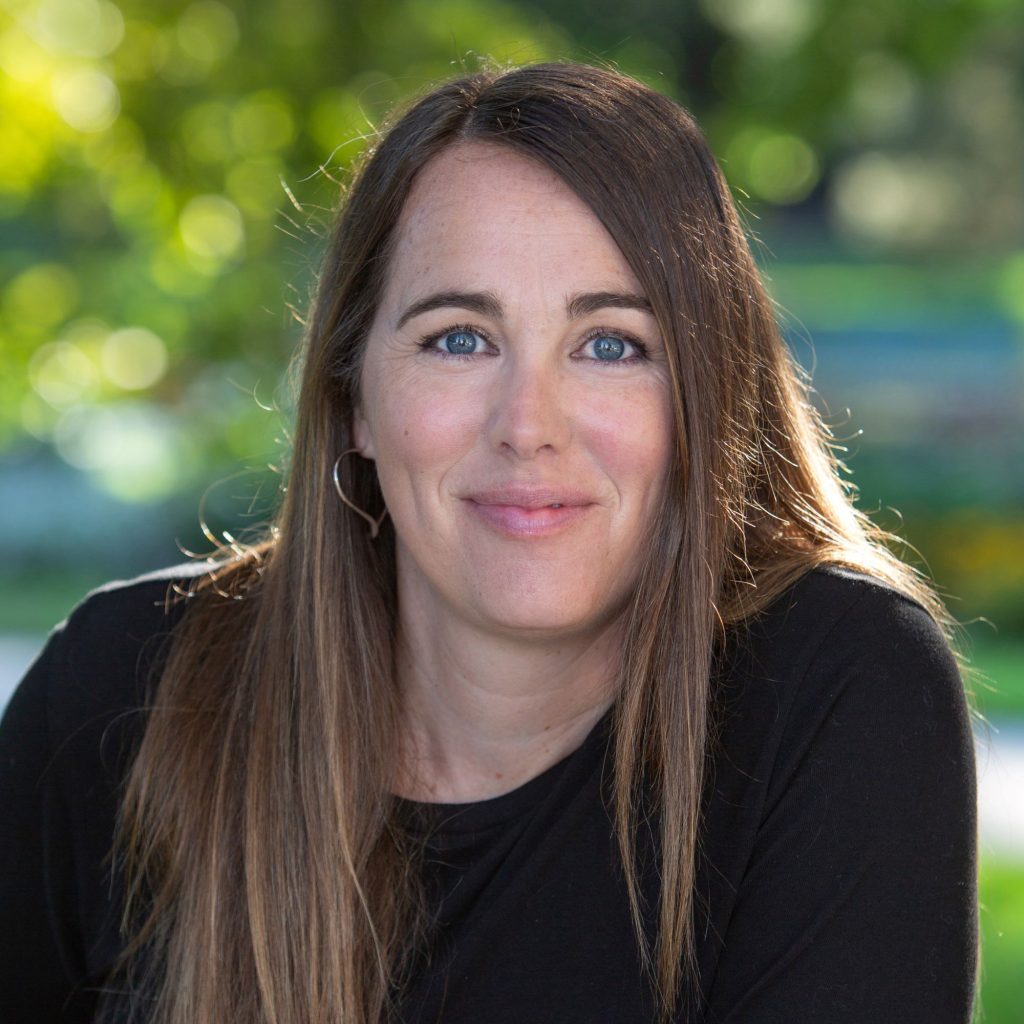 A white woman with long, light-brown hair and blue eyes wearing a black blouse smiles.