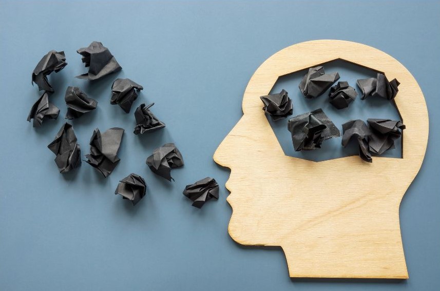 Crumpled up black pieces of paper inside a brain and some coming out of the mouth of a wooden head