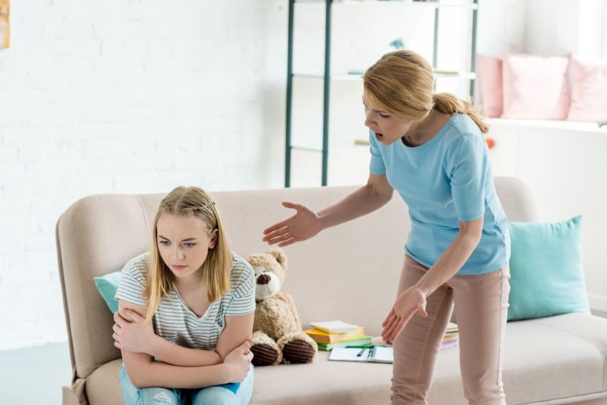 A woman standing and yelling at another woman who is looking away with her arms crossed