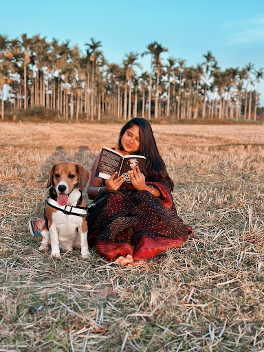 Image provided by Bookstagrammer @iambibliomane of her sitting on a field reading a book with her dog Pablo.