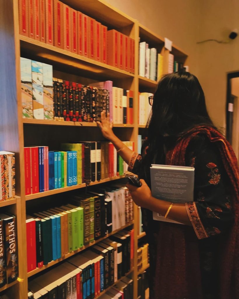 Image by @iambibliomane of the bookstagrammer picking books at a bookstore.