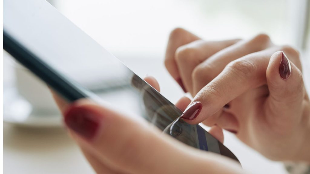 There is a close-up of a woman holding a phone in her hands and scrolling. She is wearing red nail polish.