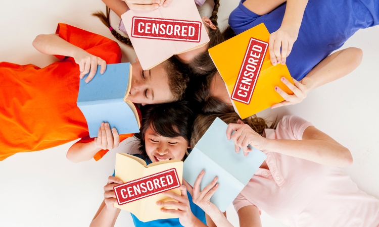 Five children are laying on their backs with their heads in a circle reading books with different colored covers. Three of the five books have a "CENSORED" badge over them.