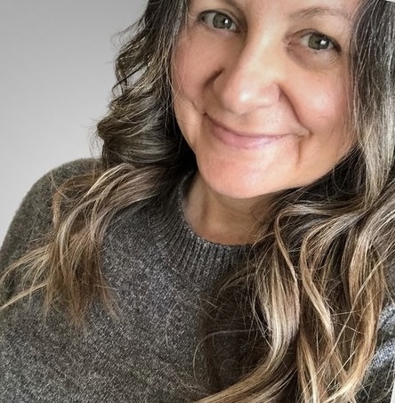 Luna Kayne wearing a gray sweater, and her hair is curling over her shoulders.