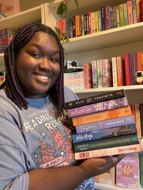 Woman holding a stack of books while standing in front of bookshelves
