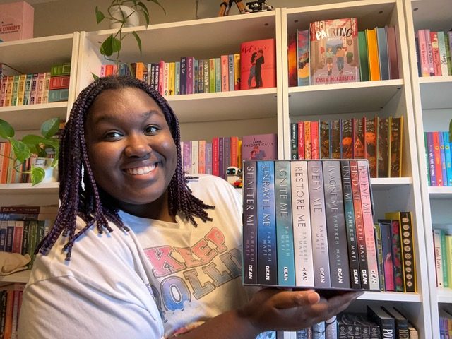 Woman holding a stack of books while standing in front of bookshelves