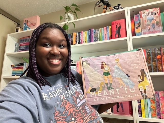Woman standing in front of a bookcase holding a pink cardboard box