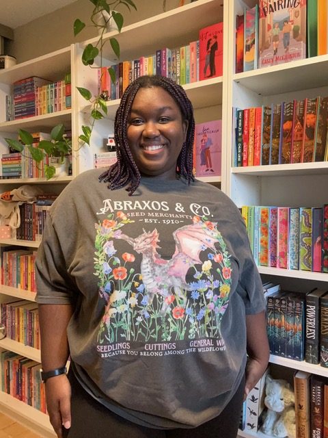 Woman wearing a gray shirt standing in front of a bookcase and smiling