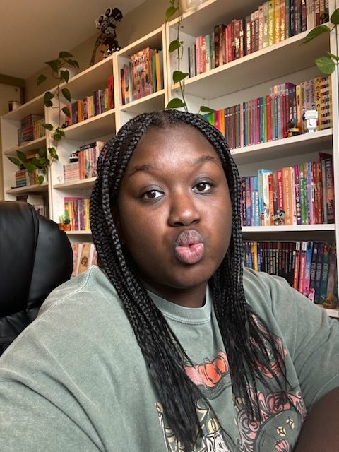 A woman wearing a green shirt posing with pouty lips while sitting in front of bookshelves