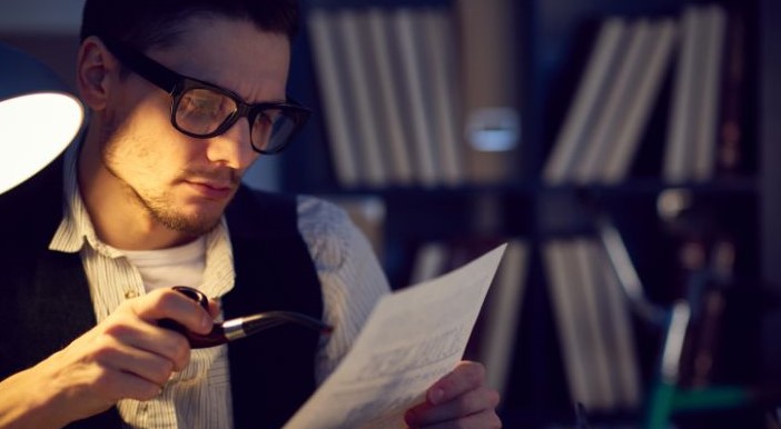 A man holding a pipe in one hand and a piece of paper in the other, staring at the paper with a confused expression.
