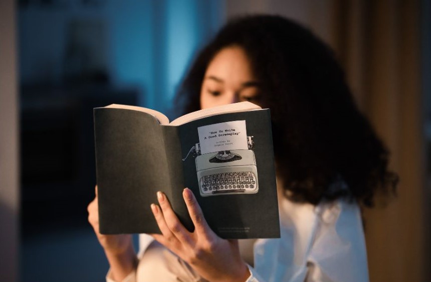 A woman reading a dark gray book called "How to Write a Good Screenplay."