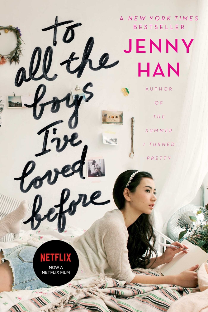 A young girl looks up as she writes in a book while laying on a bed for the cover of To All The Boys I've Loved Before.