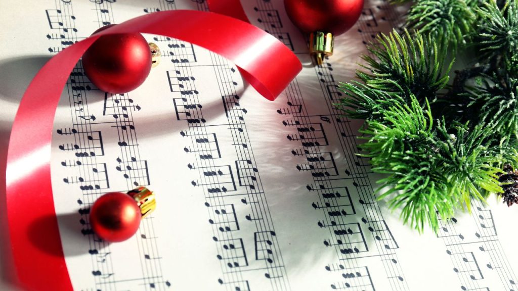 A music sheet is on a table with red string Christmas orbs and a plant.