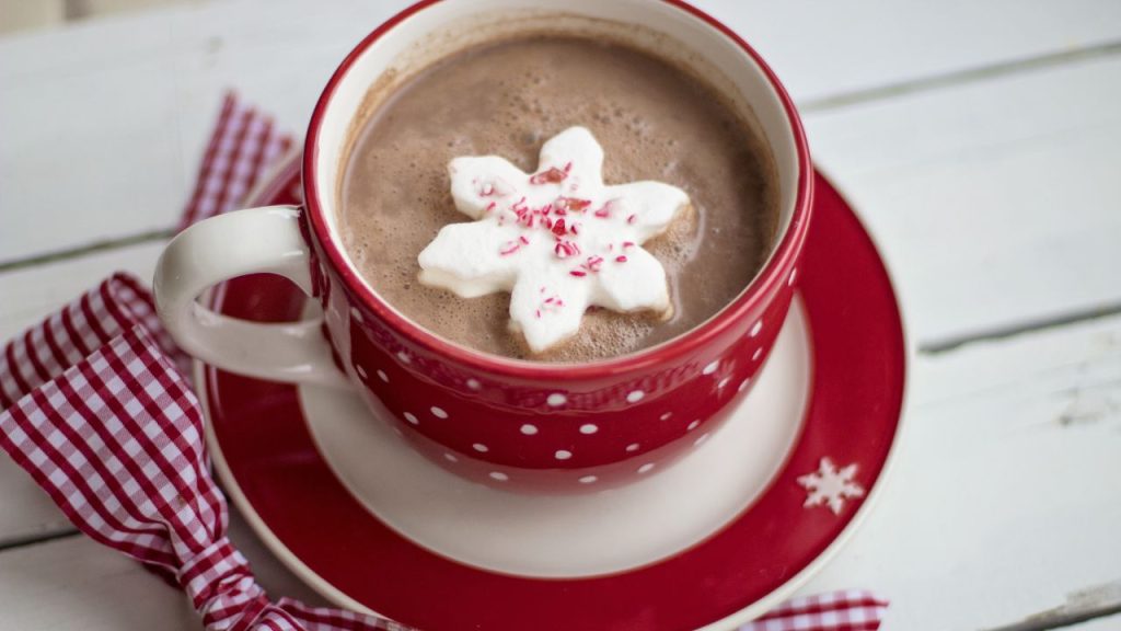 Red hot chocolate mug with matching saucer. The hot chocolate has a white cookie or marshmallow shaped like a snowflake.