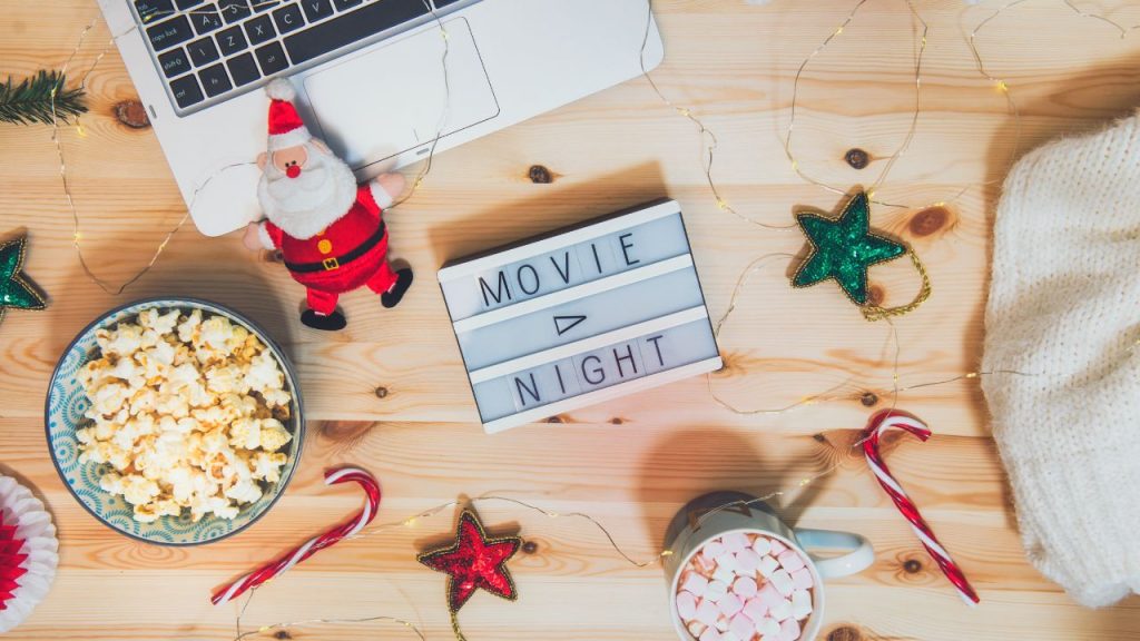 "Movie Night" light is on a table with popcorn, candy cane, and star decorations with a laptop in the corner.