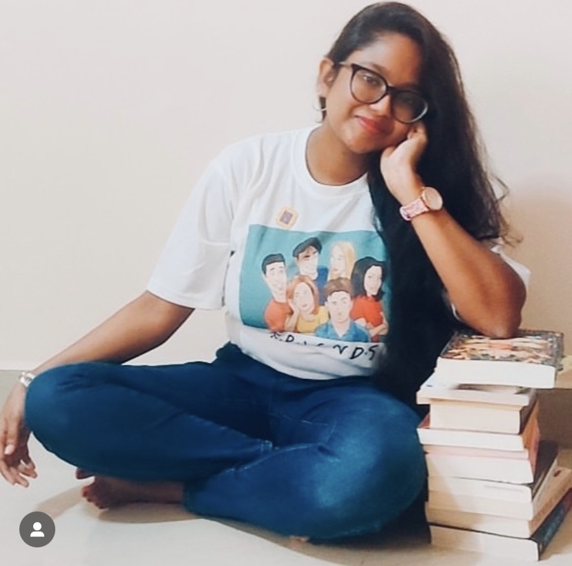Image provided by @iambibliomane of herself leaning on a stack of books on the floor.