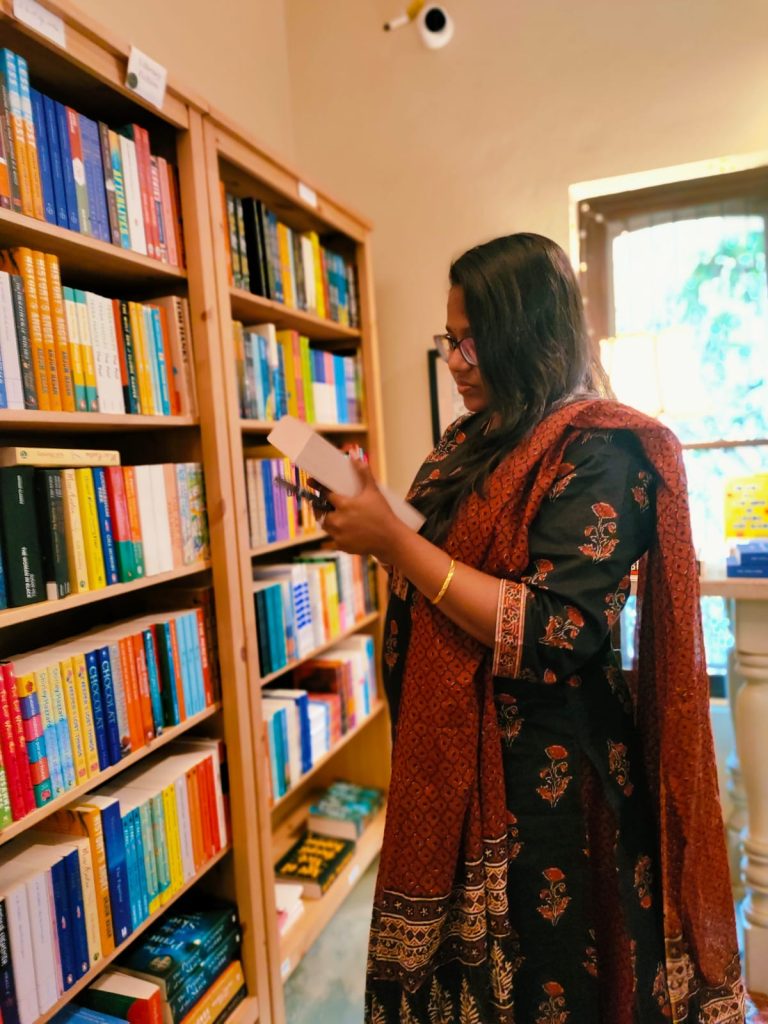 Image by @iambibliomane of Swarna looking at a book at a bookstore.