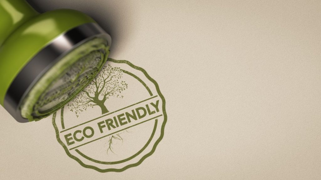 A close-up of a green stamp laying on top of off-white paper stamped with a circular pattern, a tree design, and text that reads "Eco Friendly."
