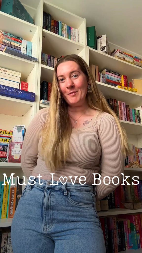 Kaitlyn is standing in front of her bookshelf, stuffed full of books.