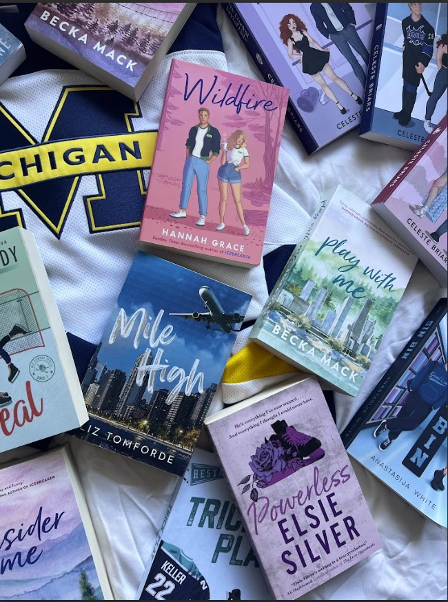 On a white bedspread is a cascade pile of books and a Michigan state jersey.