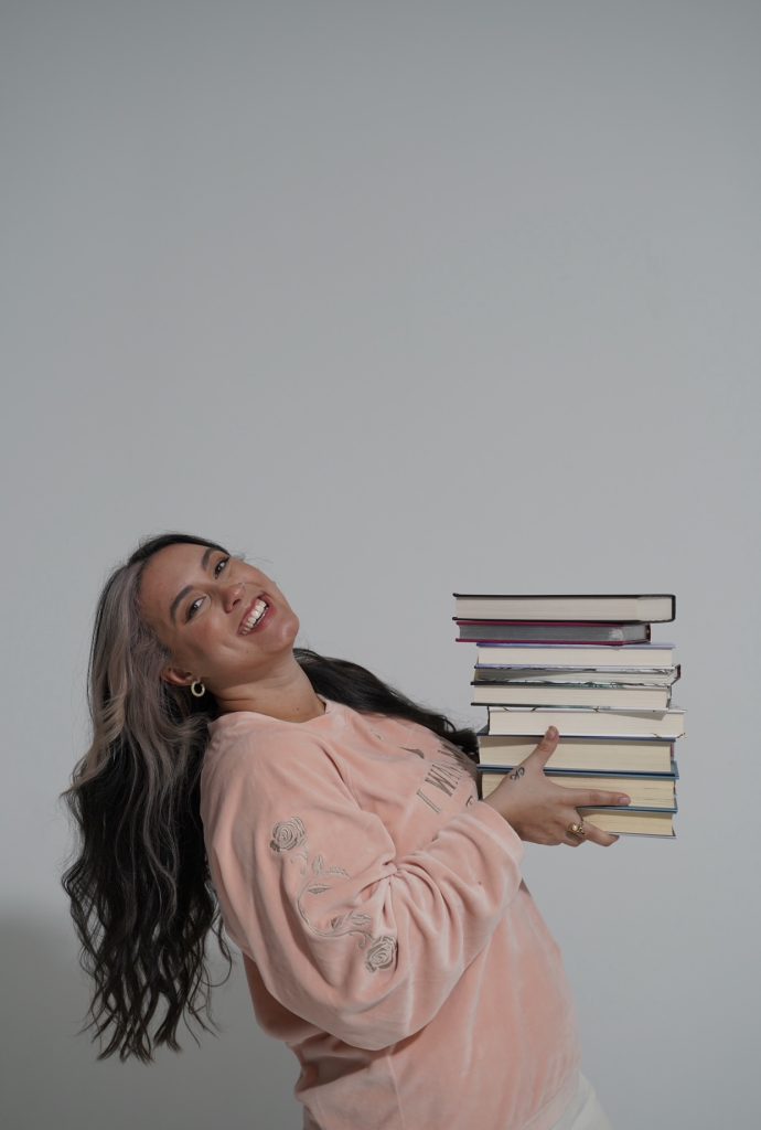 Cassandra is exuberantly happy while holding up a stack of books.