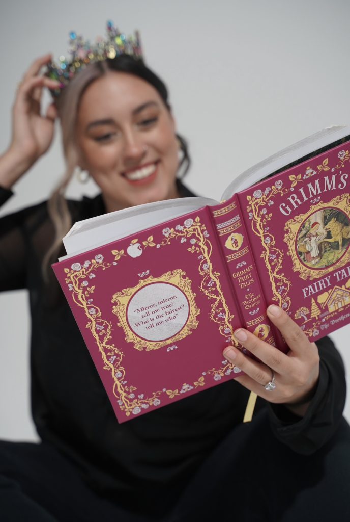 Cassandra is smiling and holding up a copy of Grimm's Fairy Tales.