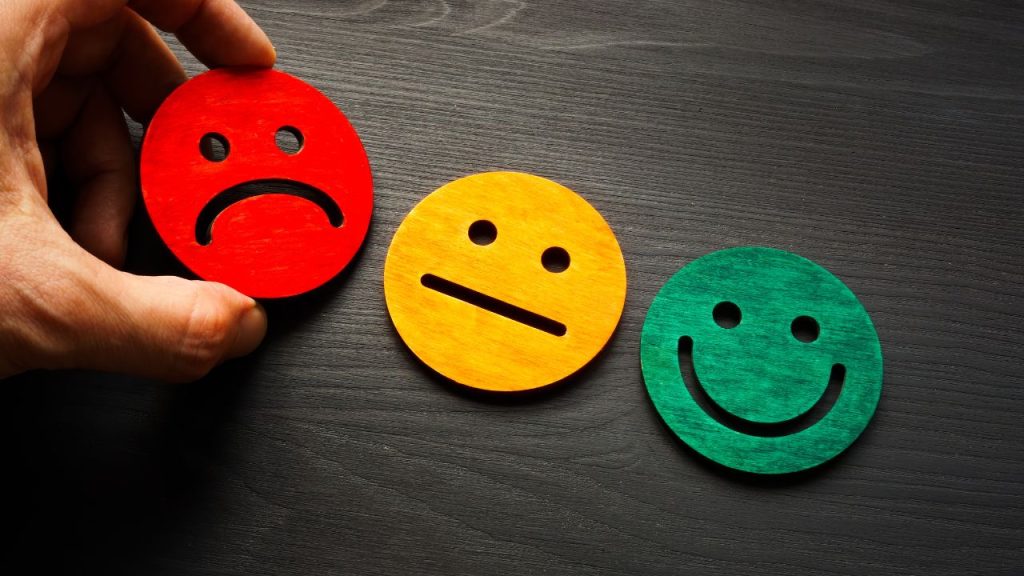 A black wood background with a red frowning face, a yellow neutral face, and a green smiling face