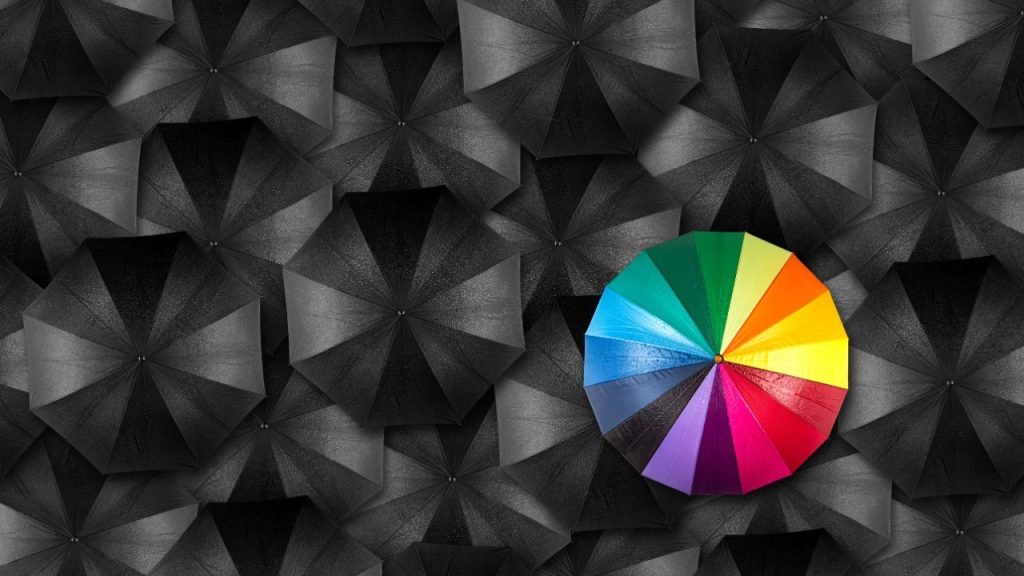 A rainbow umbrella stands out against a background of black and gray umbrellas
