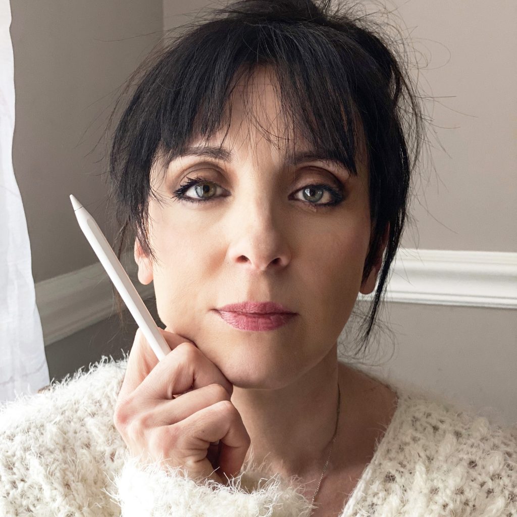 A white-skinned woman with black hair looks at the viewer with a neutral expression. She is sitting indoors new a window, wearing a white fluffy sweater and holding a digital pencil against her chin.