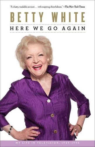 "Here We Go Again: My Life in Television" book cover with a white background and Betty White wearing a purple shirt and smiling with her hands on her hips.