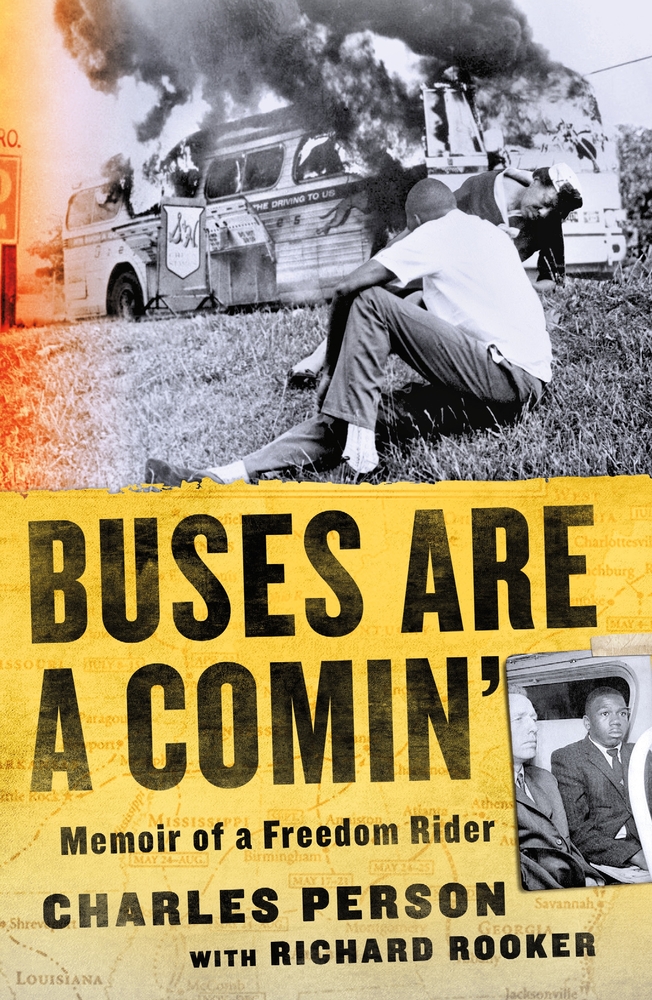 A young man, sitting on the ground, looks over his shoulder at a burning bus on the cover of Buses Are A Comin.
