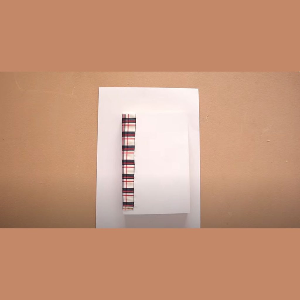 white paper cardboard book cover with a strip of fabric on the spine sitting on top of a plain sheet of white paper with a brown background