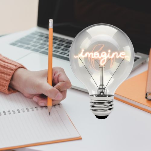 a hand holding a pencil about to write in a notebook with an open laptop and a lightbulb that says imagine is glowing letters
