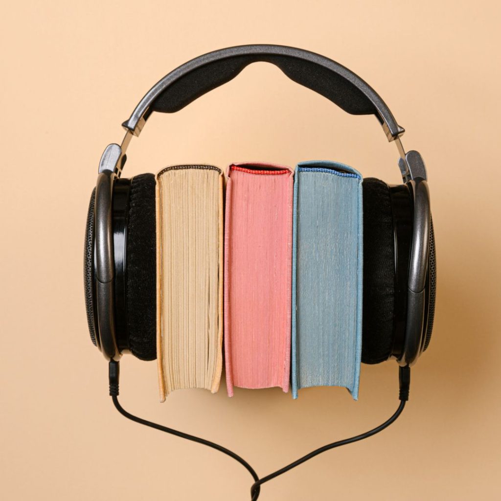 Orange background with black headphones covering three books. One orange, one red, and one blue book.